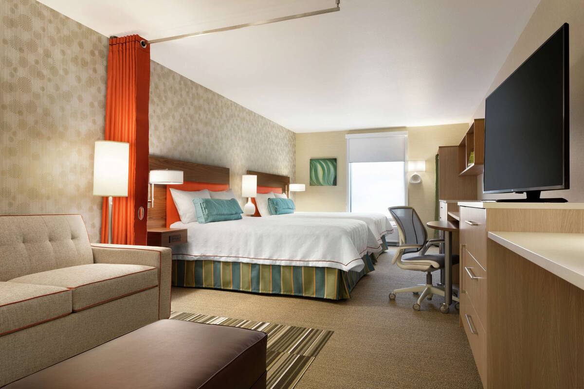 A hotel room with a bed, a desk, a chair, a TV, and a sofa.