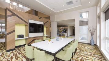 Una habitación de hotel moderna con una amplia mesa de comedor, asientos cómodos, un televisor de pantalla plana y un detalle decorativo en la pared.