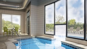 Una piscina interior con agua cristalina, ventanas amplias y sillas verdes.