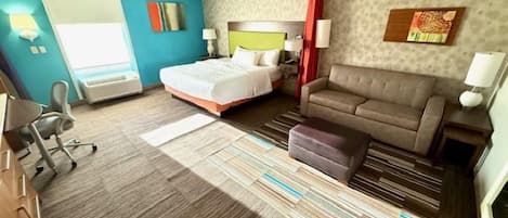 A hotel room with a bed, a sofa, a desk, and a chair.
