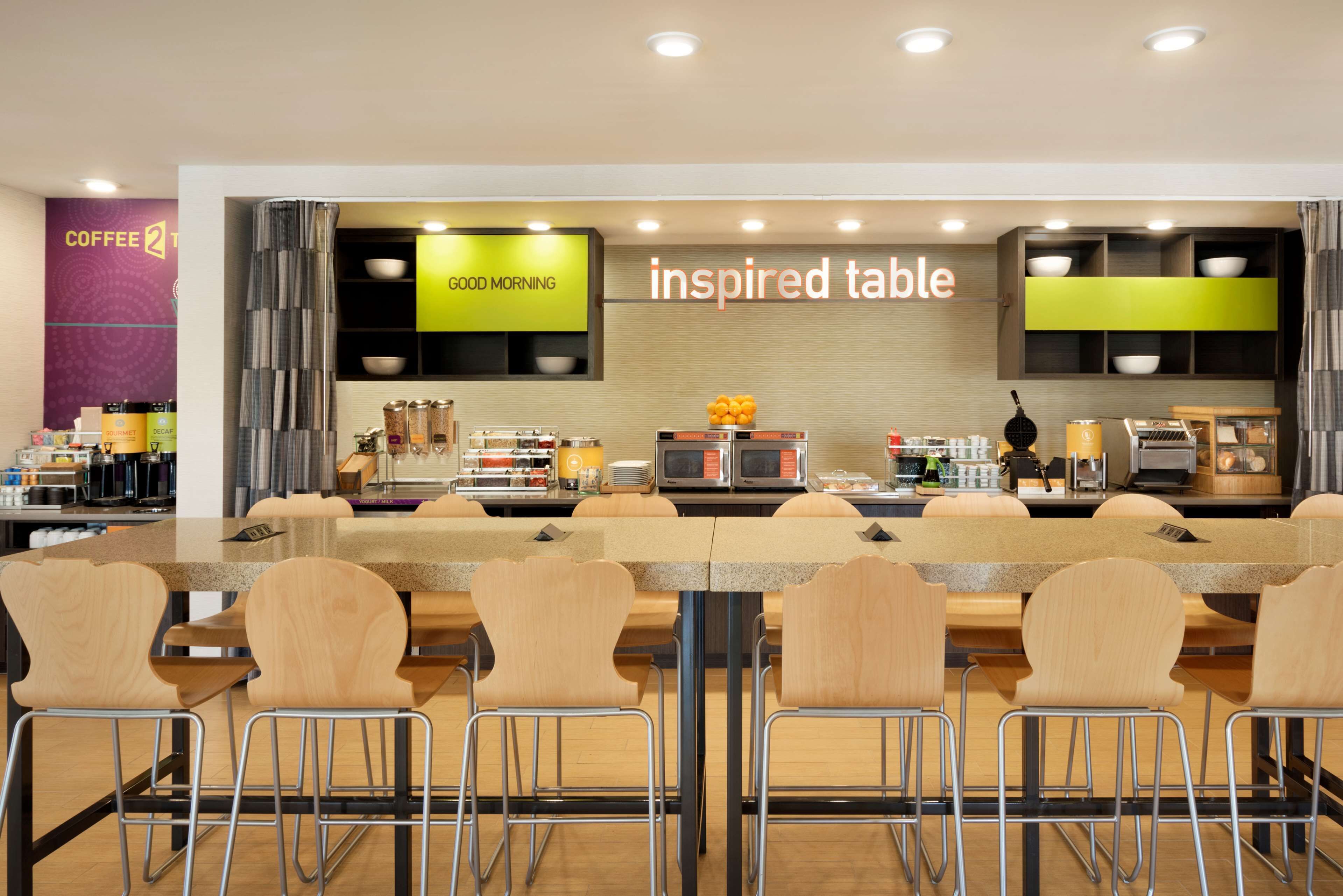 A modern cafe with a long communal table, bar stools, and a variety of coffee-making equipment.