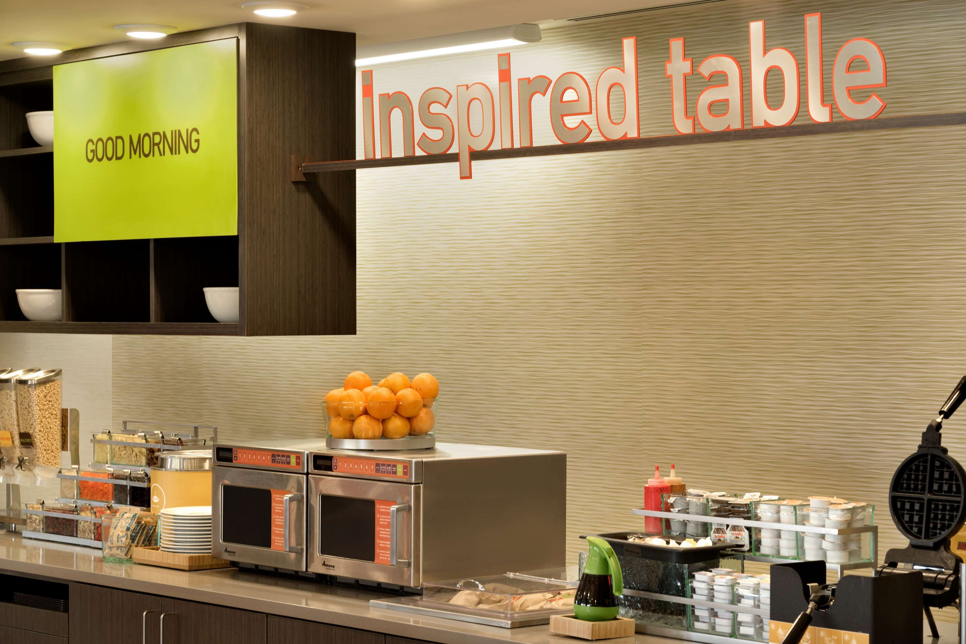 Zona de desayuno tipo buffet con un letrero que dice "Inspired table" y un cartel con la frase "Buenos días" arriba.