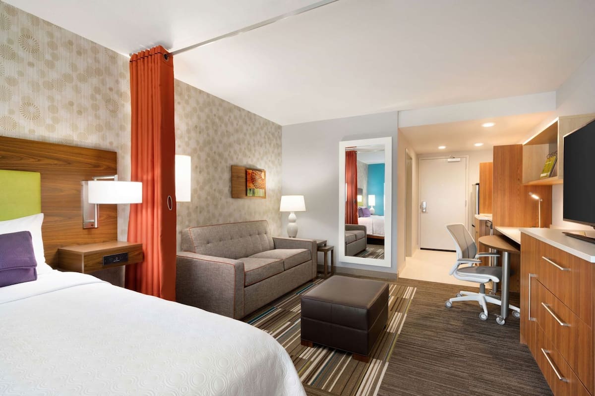 A hotel room with a bed, sofa, desk, chair, and a television.