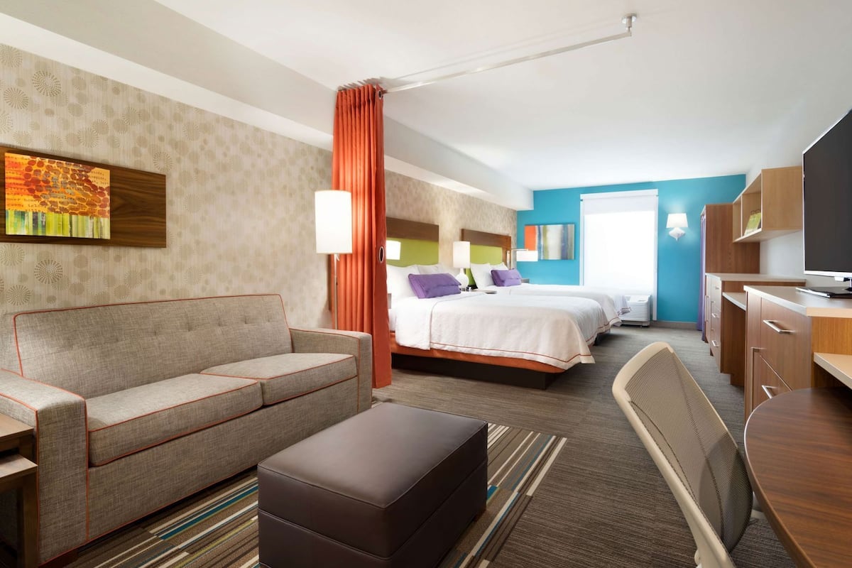 A hotel room with a sofa, two beds, a desk, and a TV.