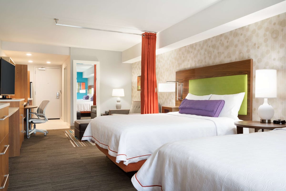 A hotel room with two beds, a desk, a chair, and a TV.