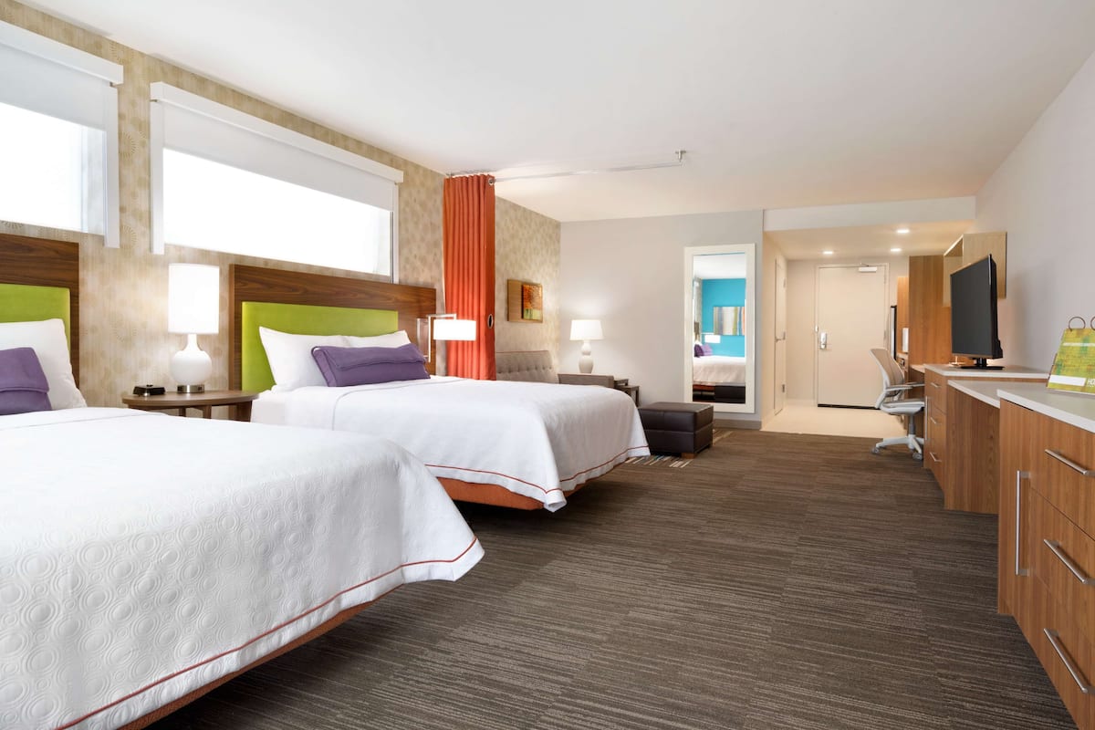 A hotel room with two beds, a desk, a TV, and a bathroom visible through an open door.