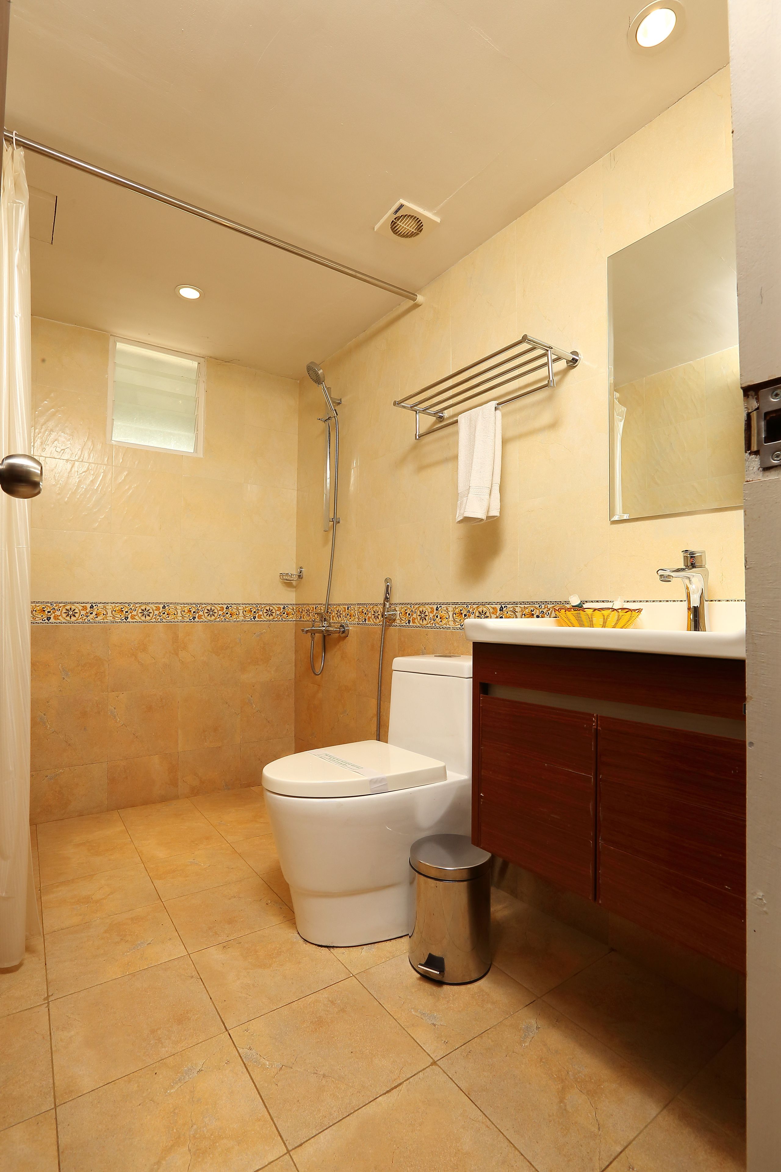 A bathroom with a shower, toilet, sink, and a trash can.