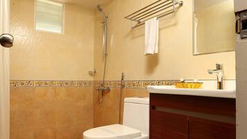 A bathroom with a shower, toilet, sink, and a trash can.