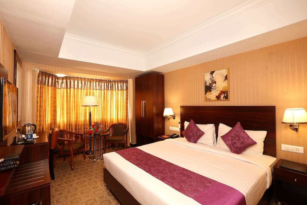 Quarto de hotel com uma cama grande, duas luminárias laterais, uma escrivaninha com um computador, uma cadeira e uma luminária de mesa.