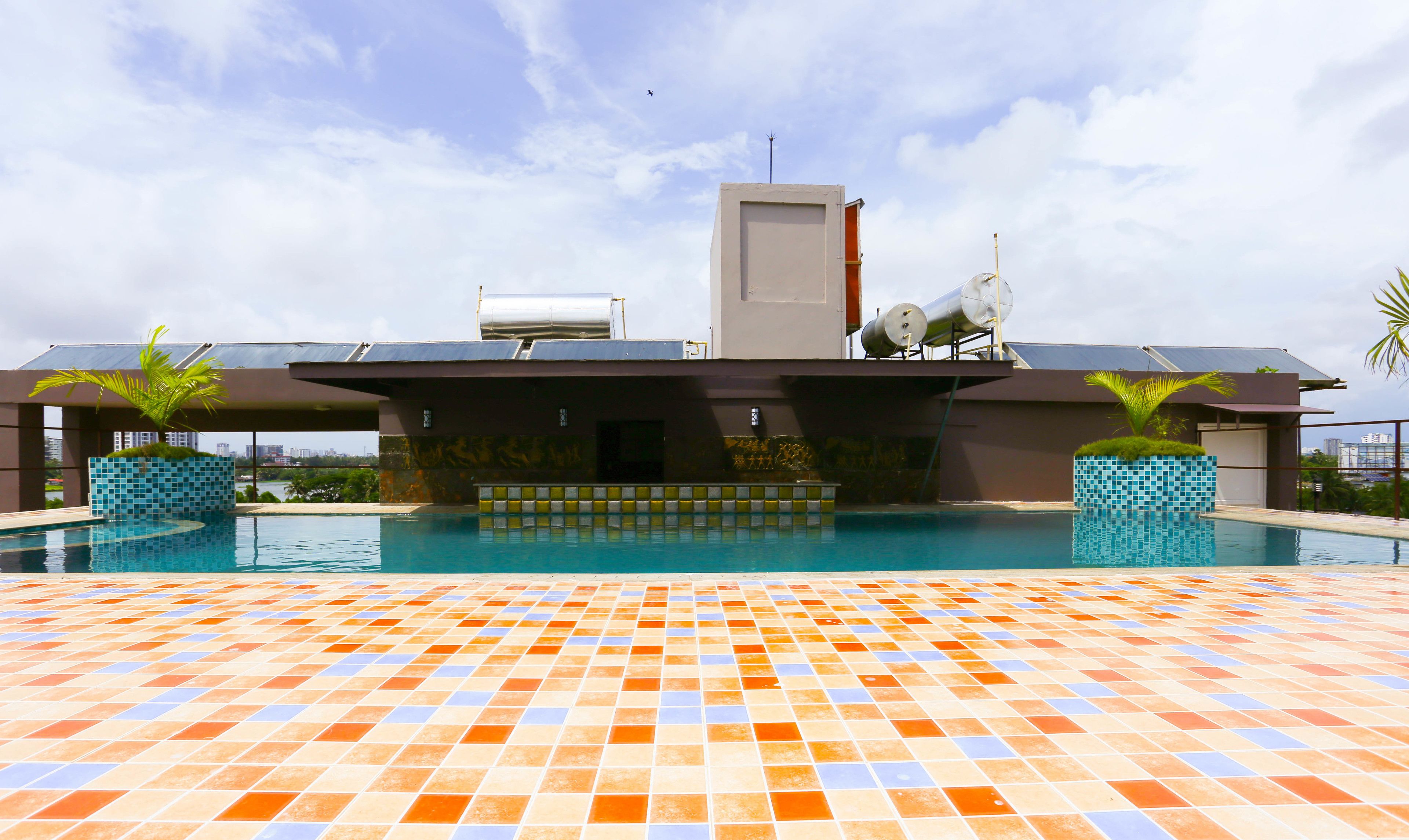 Una piscina en la azotea con suelo de baldosas y un edificio moderno al fondo.