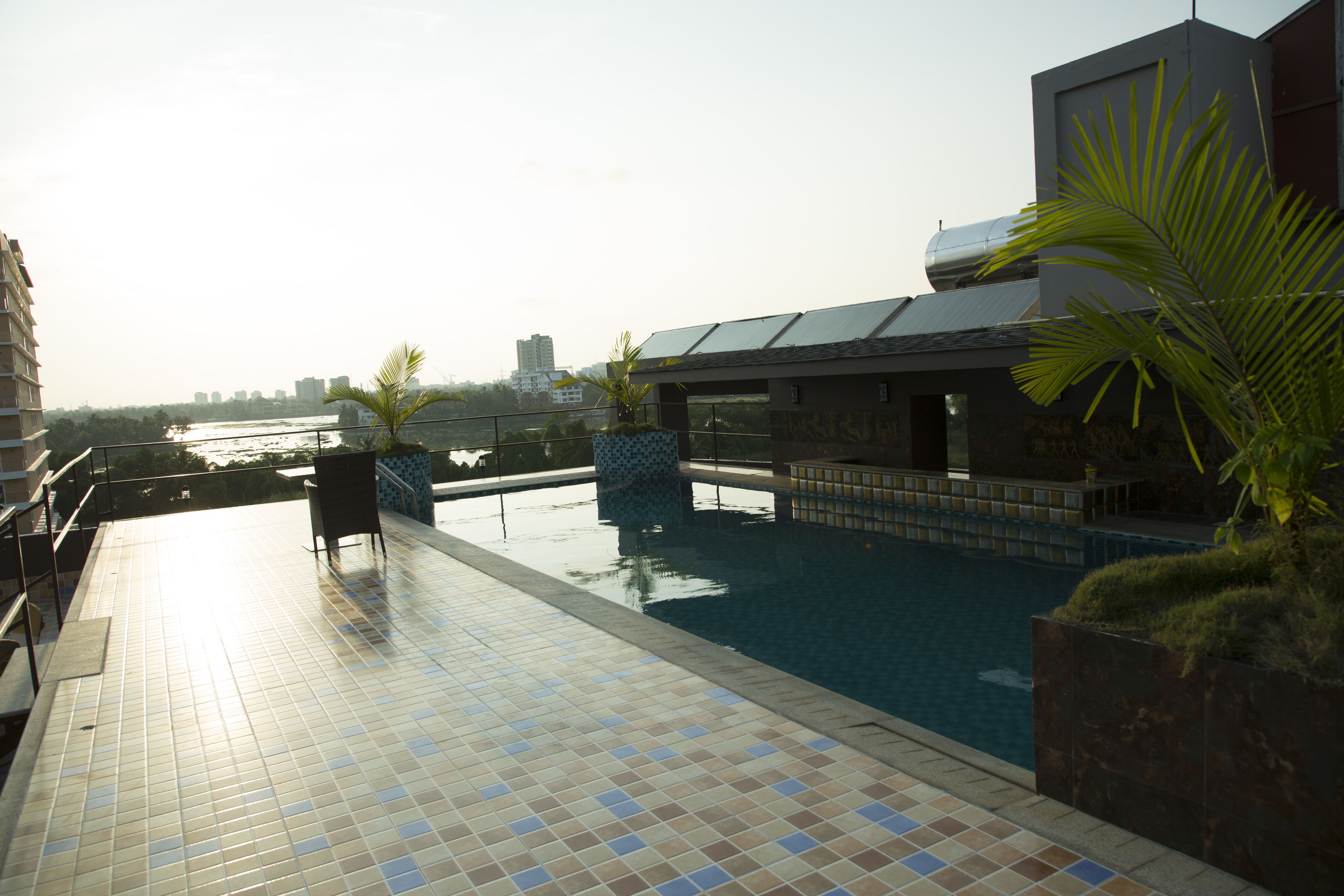 A rooftop swimming pool with tiled flooring, a seating area, and a view of the city skyline.