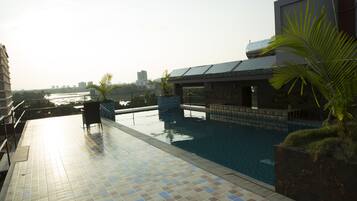 A rooftop swimming pool with tiled flooring, a seating area, and a view of the city skyline.