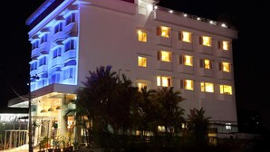 Un hotel con un llamativo letrero de neón que dice “LEGACY HOTEL” en la parte superior. El edificio cuenta con varios balcones y ventanas con iluminación cálida en el interior.