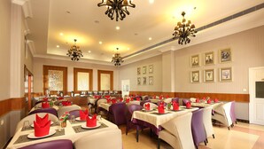 Un comedor con mesas dispuestas para varios comensales, con sillas moradas y color beige, y un candelabro.