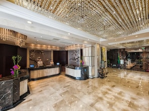 Een hotelhal met marmeren vloeren, een receptiebalie en een decoratief plafond.