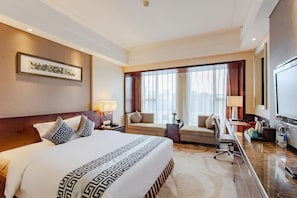 A hotel room with a large bed, a sofa, a desk, and a TV.