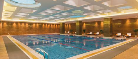 A large indoor swimming pool with clear lane markings, surrounded by lounge chairs and a modern ceiling design.