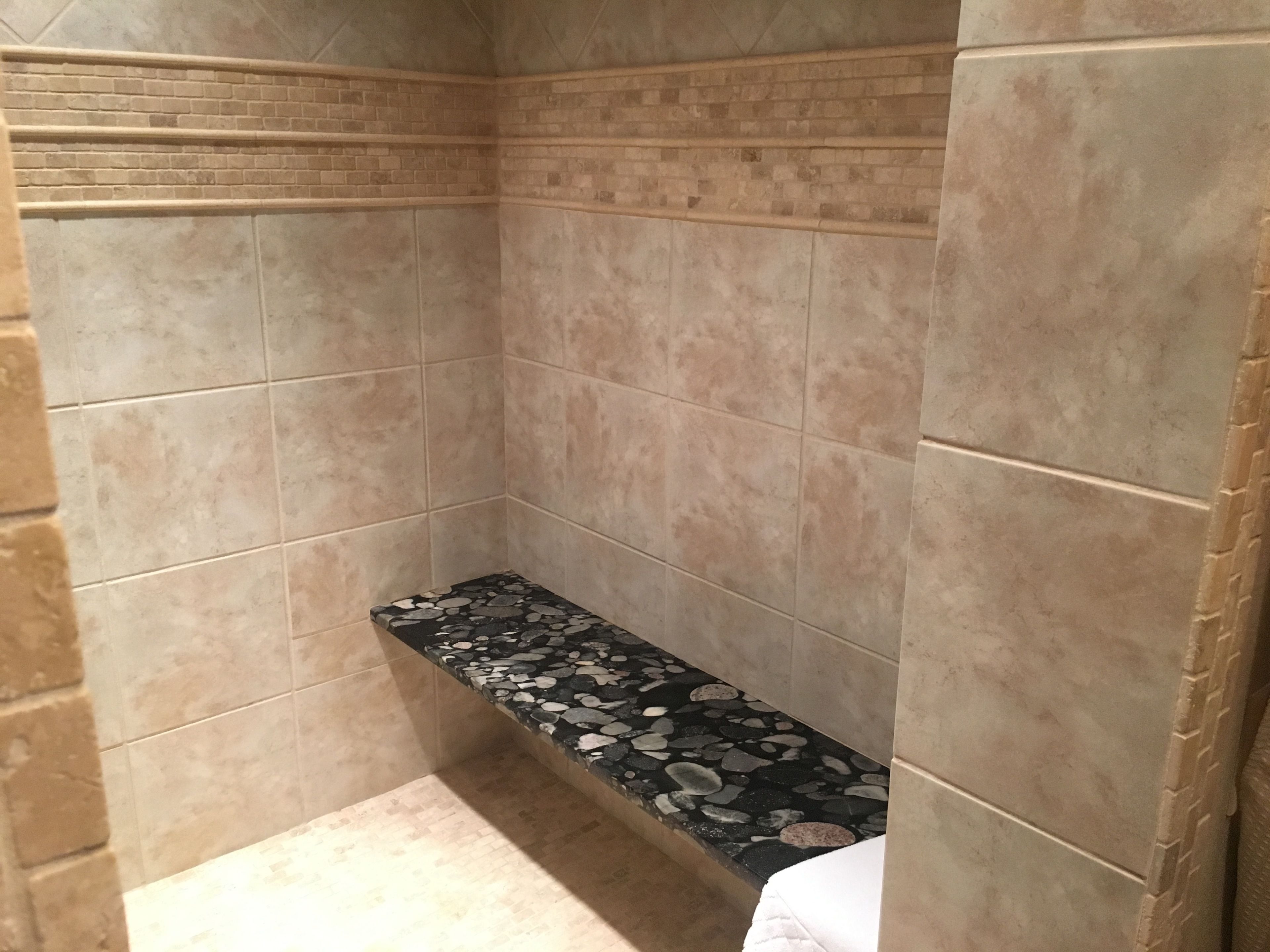 A bathroom with beige tiles, a stone shelf, and a white towel.