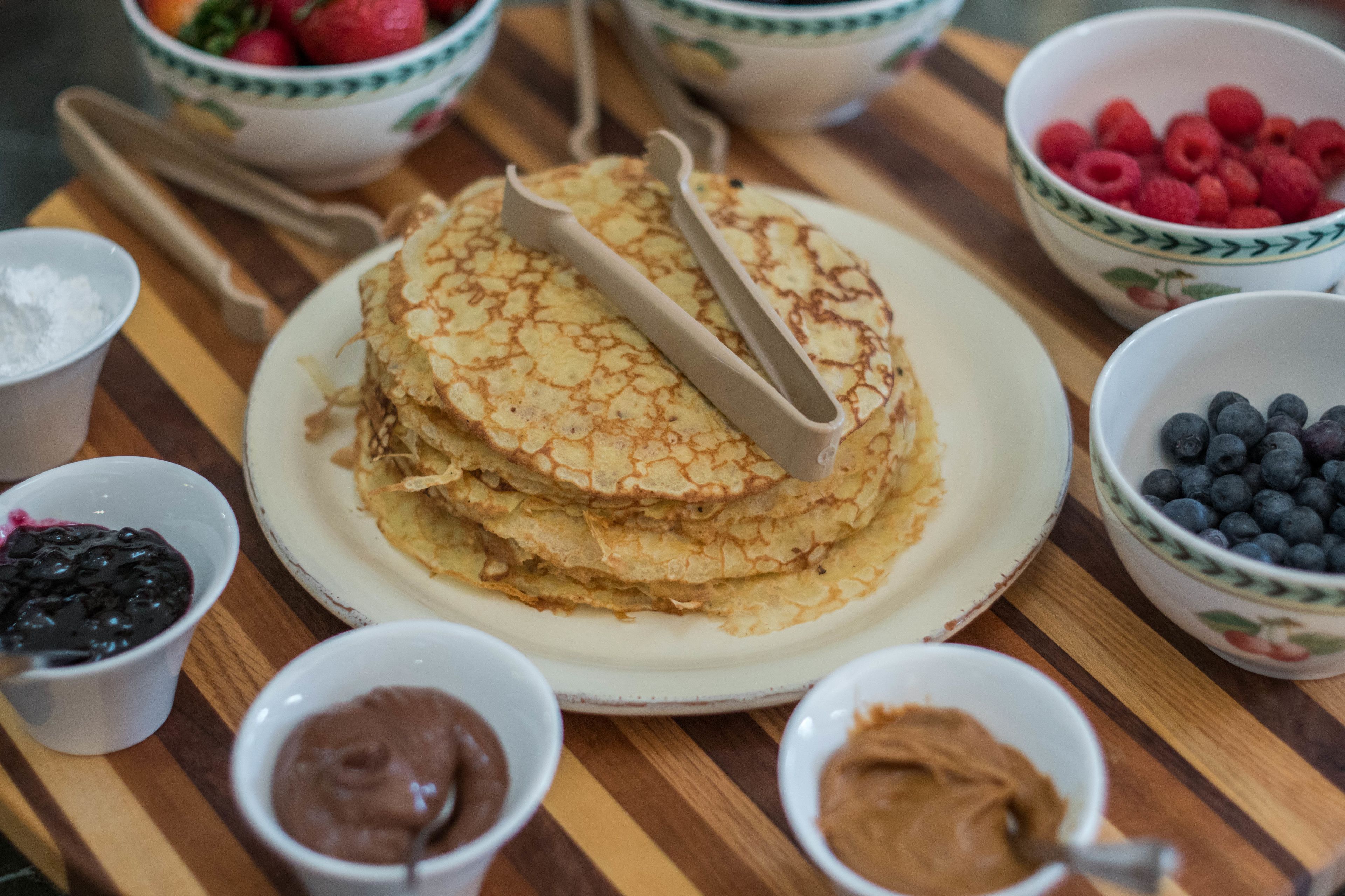 En hög med pannkakor på en tallrik, serverade med olika tillbehör och tillval.