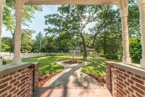 A covered walkway with brick walls and a central garden area, leading to a white picket fence and houses in the background. - The Victoria B & B (Bentonville)