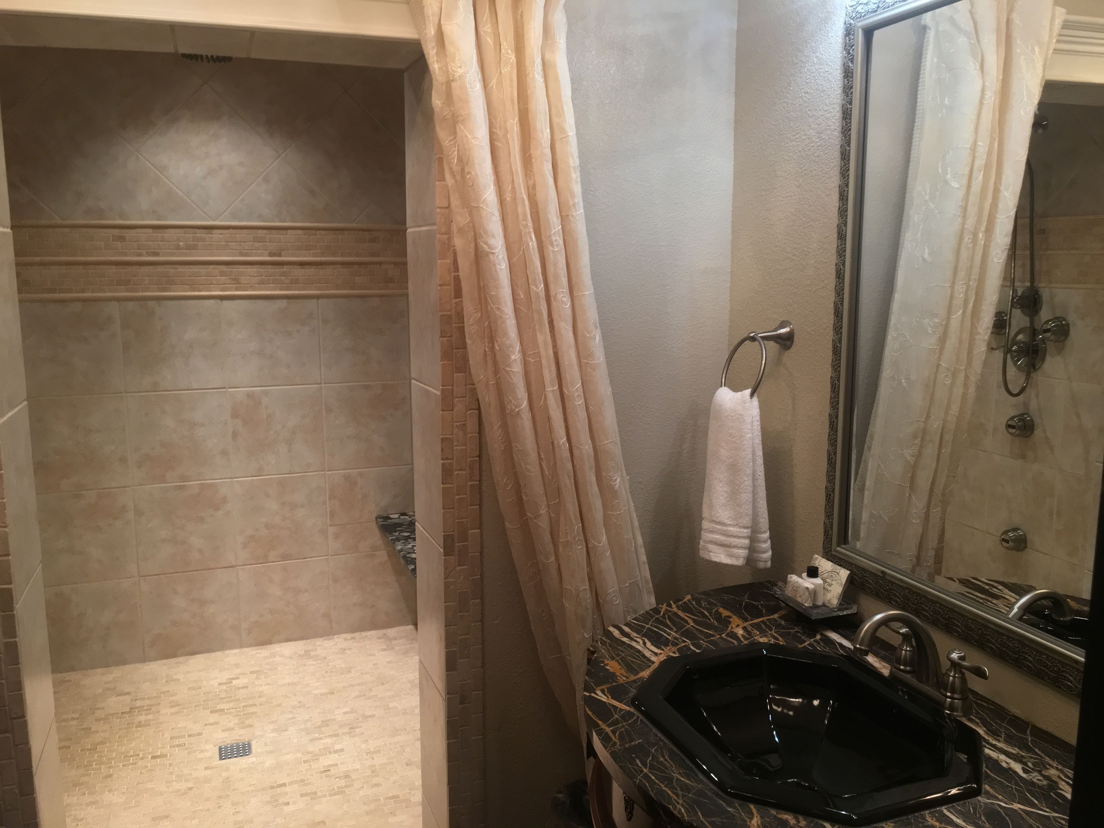 Casa de banho com chuveiro, pia com bancada de mármore e toalha pendurada num porta-toalhas.