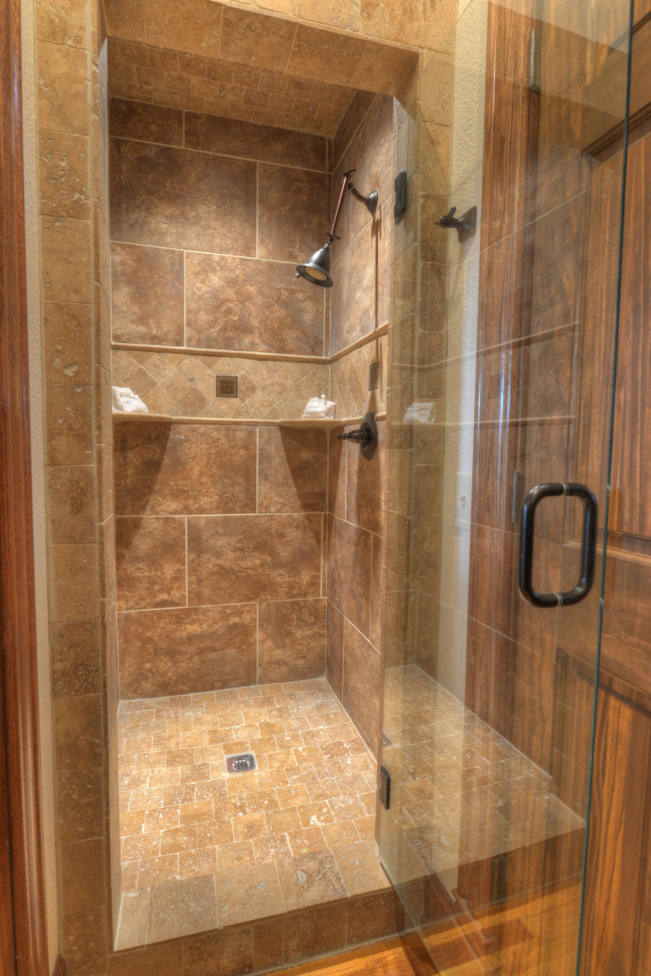 A glass-enclosed shower with a tiled floor and a wooden door.