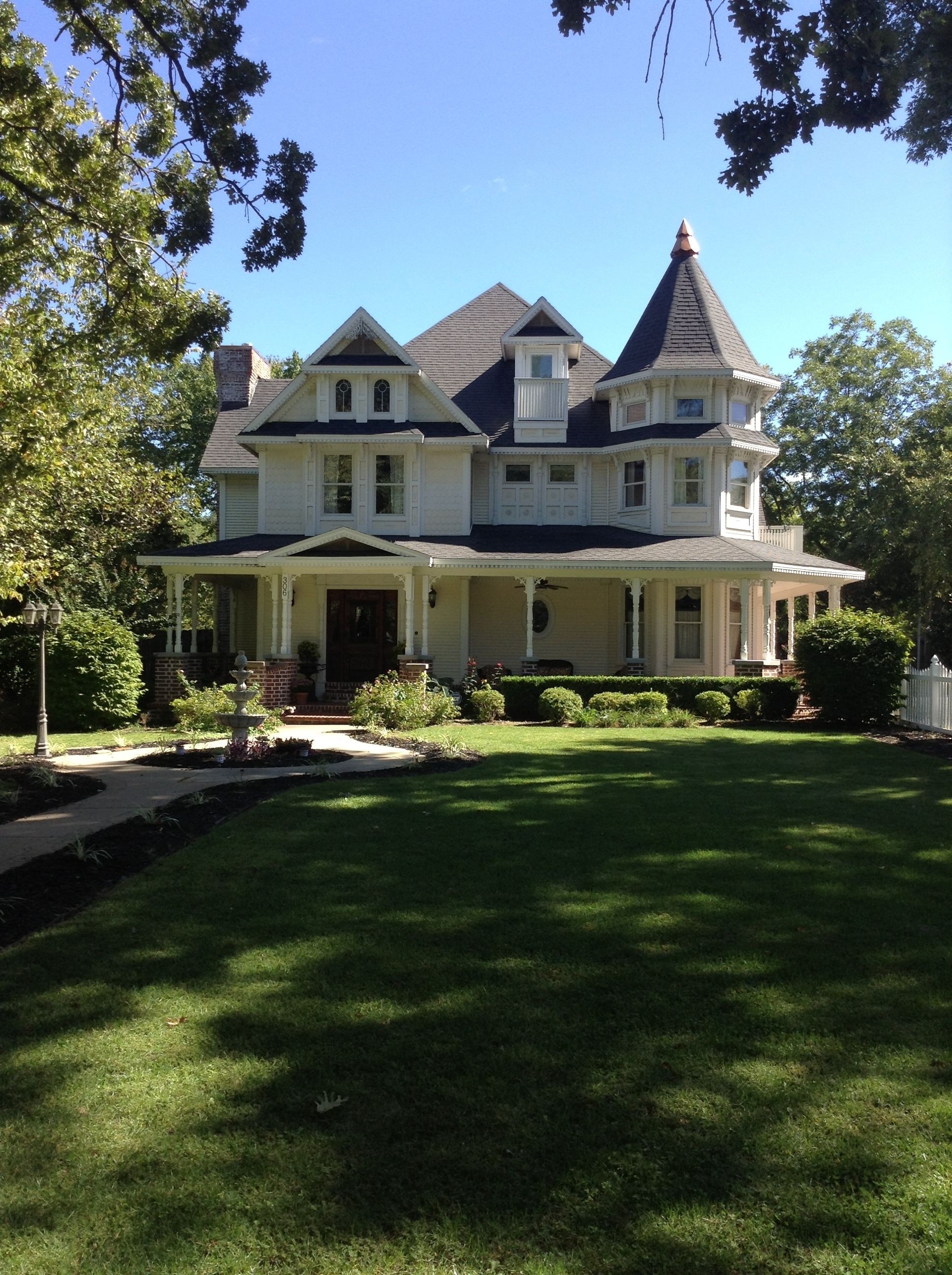 A large, two-story house with a wrap-around porch, multiple windows, and a prominent tower.