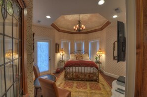 A bedroom with a large bed, two bedside lamps, a chandelier, a wooden ceiling, and a large window. - The Victoria B & B (Bentonville)