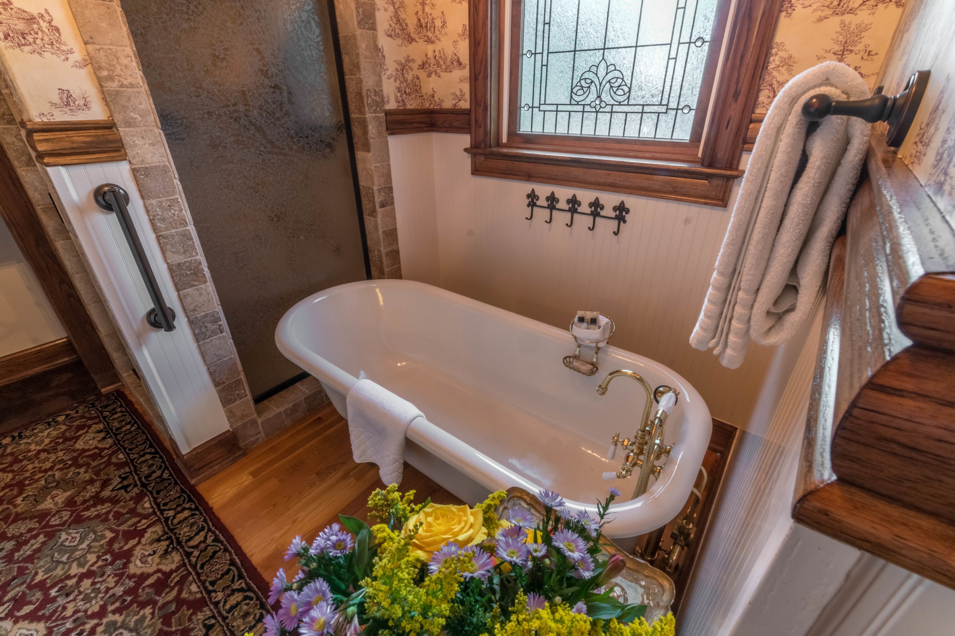 Une salle de bain avec une baignoire blanche, une fenêtre ornée d’une grille décorative et un porte-serviettes avec des serviettes.
