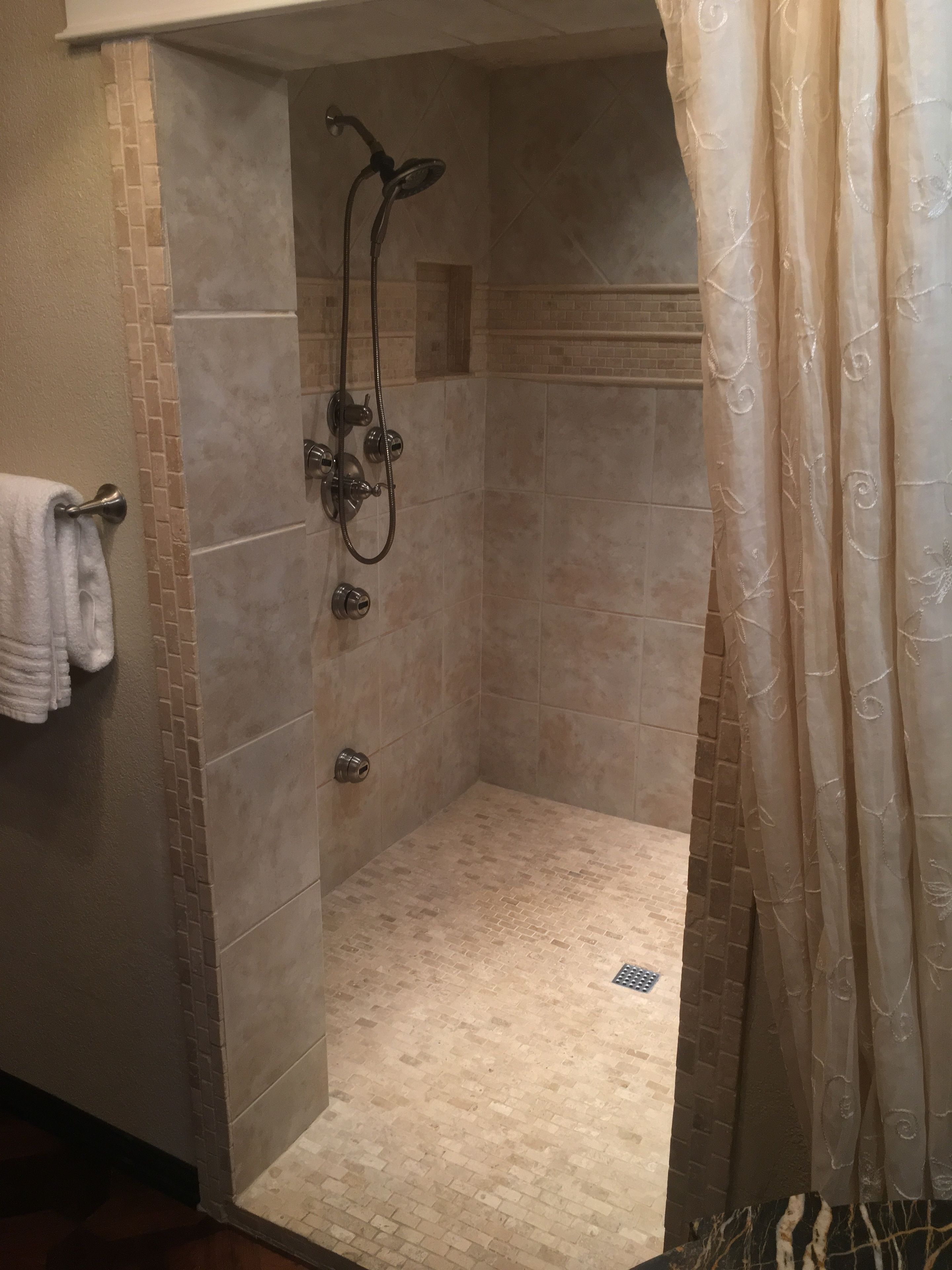 A shower area with a tiled floor, a showerhead, and a curtain.