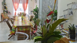 A dining area with a long table, chairs, and potted plants. - Résidence Plocus (Fort-de-France)