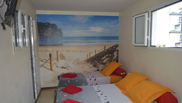 A room with two beds, each with red and orange pillows, and a beach mural on the wall. - Résidence Plocus (Fort-de-France)