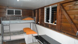A bunk bed with an orange pillow, a desk with a chair, and a window with metal bars. - Résidence Plocus (Fort-de-France)