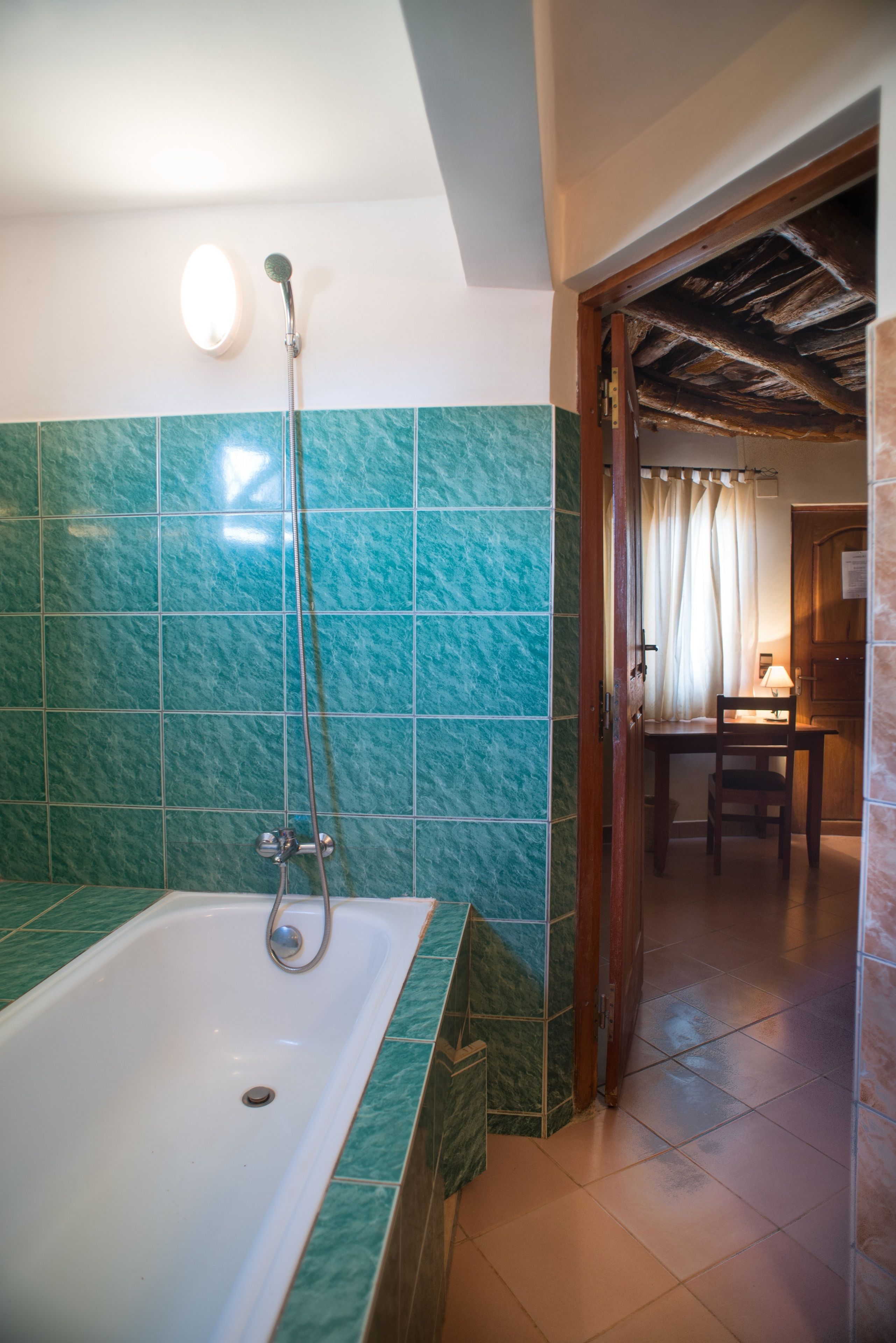 A bathroom with a bathtub, a shower, and a wooden door leading to a dining area.