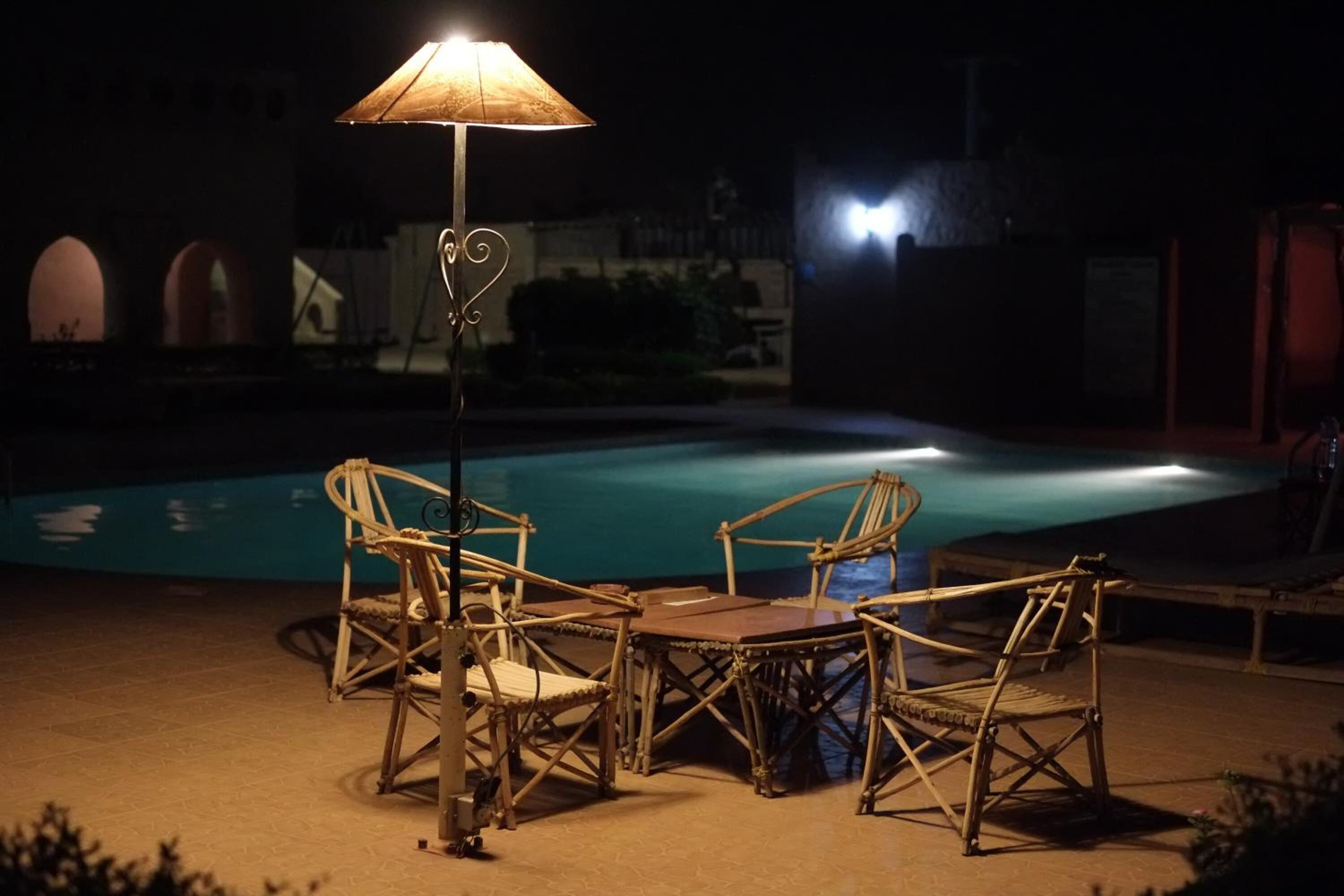 A poolside area with wicker furniture and a table, surrounded by a pool.