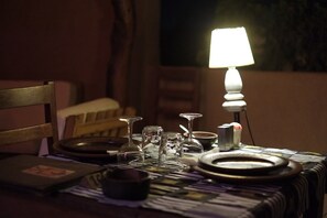 A dimly lit dining table with plates, glasses, and a candle holder, set against a dark background.