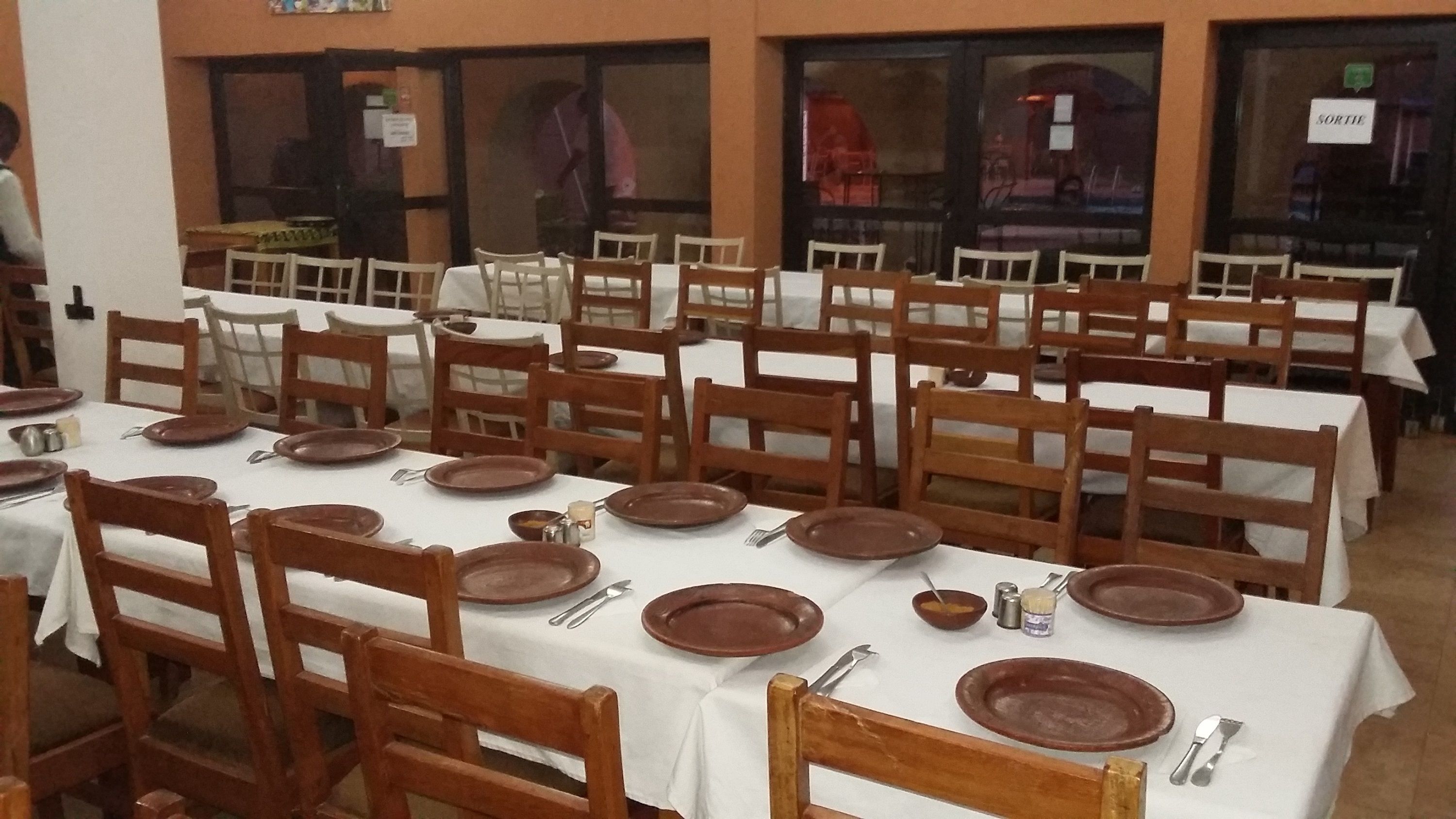 A dining hall with multiple tables set with brown plates, white tablecloths, and wooden chairs.