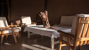 A rustic room with wooden furniture, including a sofa and chairs, a table with a white tablecloth, and a wooden sculpture. - Le Grand Calao (Ouagadougou)