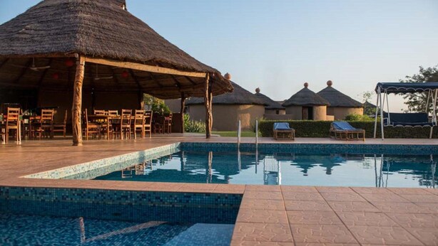 A pool area with a thatched-roof pavilion, lounge chairs, and a tiled deck. - Le Grand Calao (Ouagadougou)