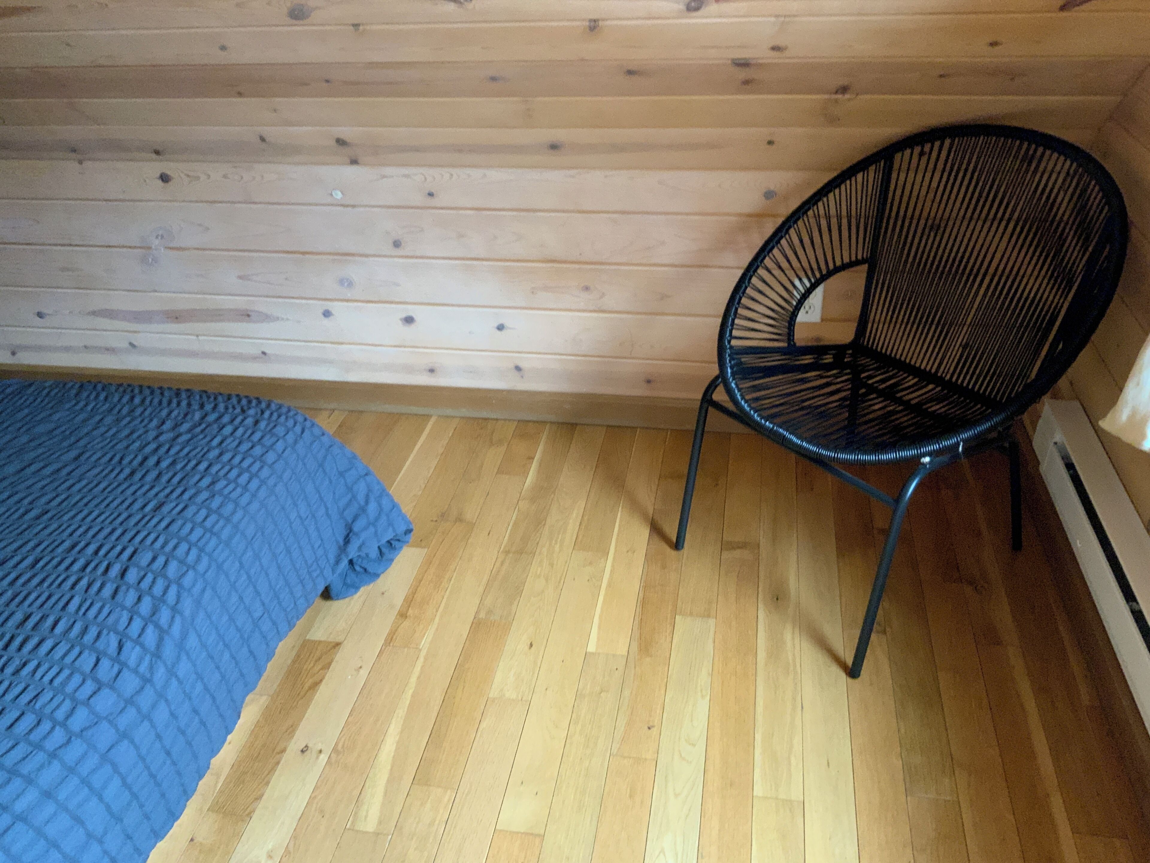 A room with a wooden floor, a blue bedspread, and a black chair.