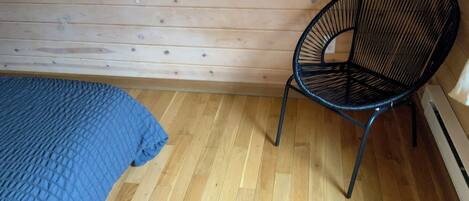 A room with a wooden floor, a blue bedspread, and a black chair.