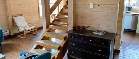 A wooden interior with a staircase, a rocking chair, a sofa, and a dresser.