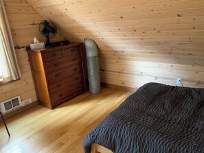 A room with a wooden ceiling, a wooden dresser, a mattress, and a wall-mounted fan. - Rolling Huts (Winthrop)