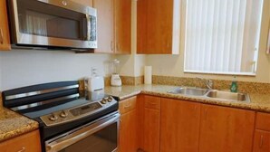 A kitchen with wooden cabinets, a stainless steel oven, a microwave, a sink, and a window with blinds. - Miami Luxury Suite in Downtown Brickell (Miami)