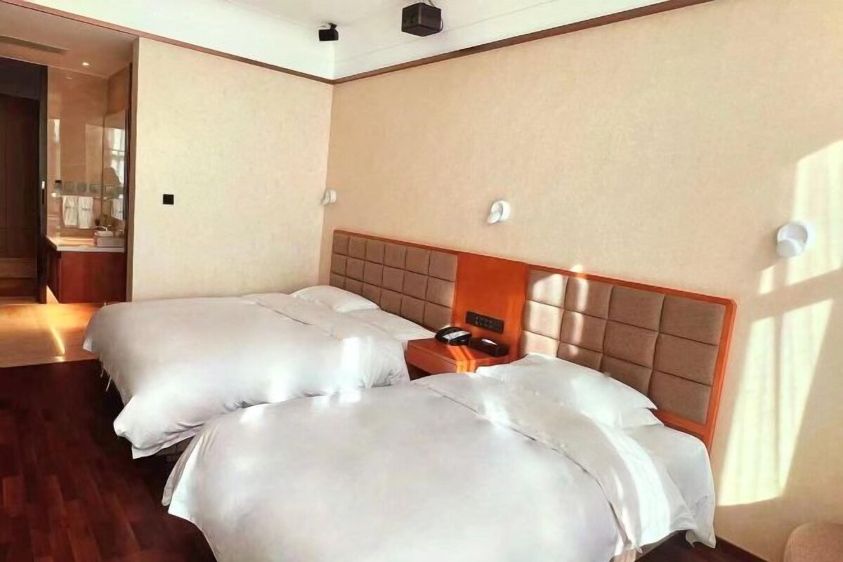 Una habitación de hotel con dos camas, cabeceros de madera, mesitas de noche y un espejo.