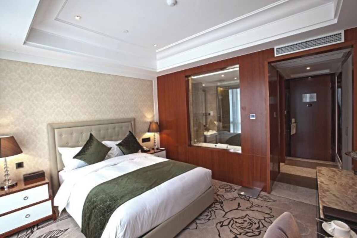 Ein Hotelzimmer mit einem großen Bett, einem Nachttisch, einem Spiegel und einer Tür zu einem Badezimmer.