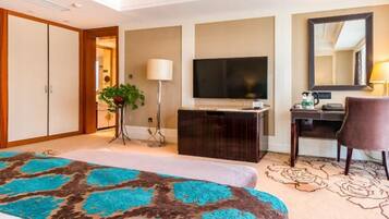 Habitación de hotel con cama, escritorio, televisión, espejo y planta.