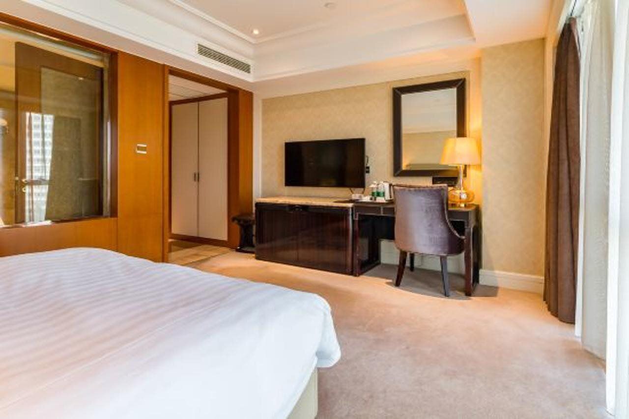 A hotel room with a large bed, a desk with a computer and lamp, a TV, and a wardrobe.
