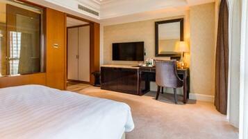 A hotel room with a large bed, a desk with a computer and lamp, a TV, and a wardrobe.