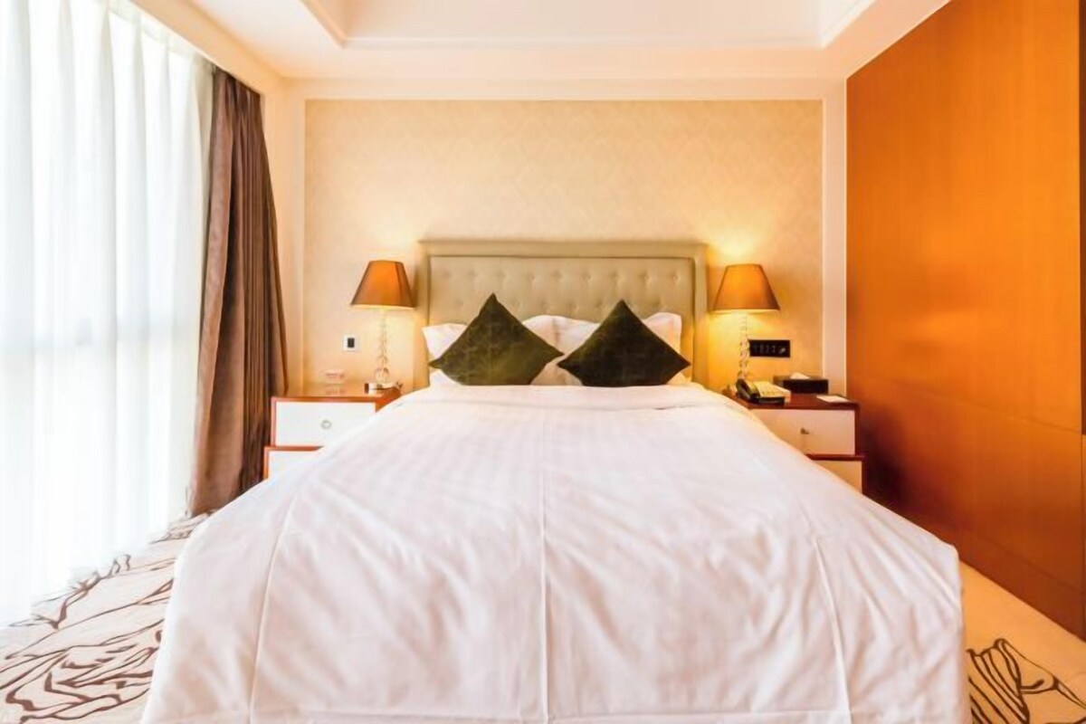 Habitación de hotel con una cama grande, dos lámparas de noche, una mesita de noche y una ventana con cortinas.